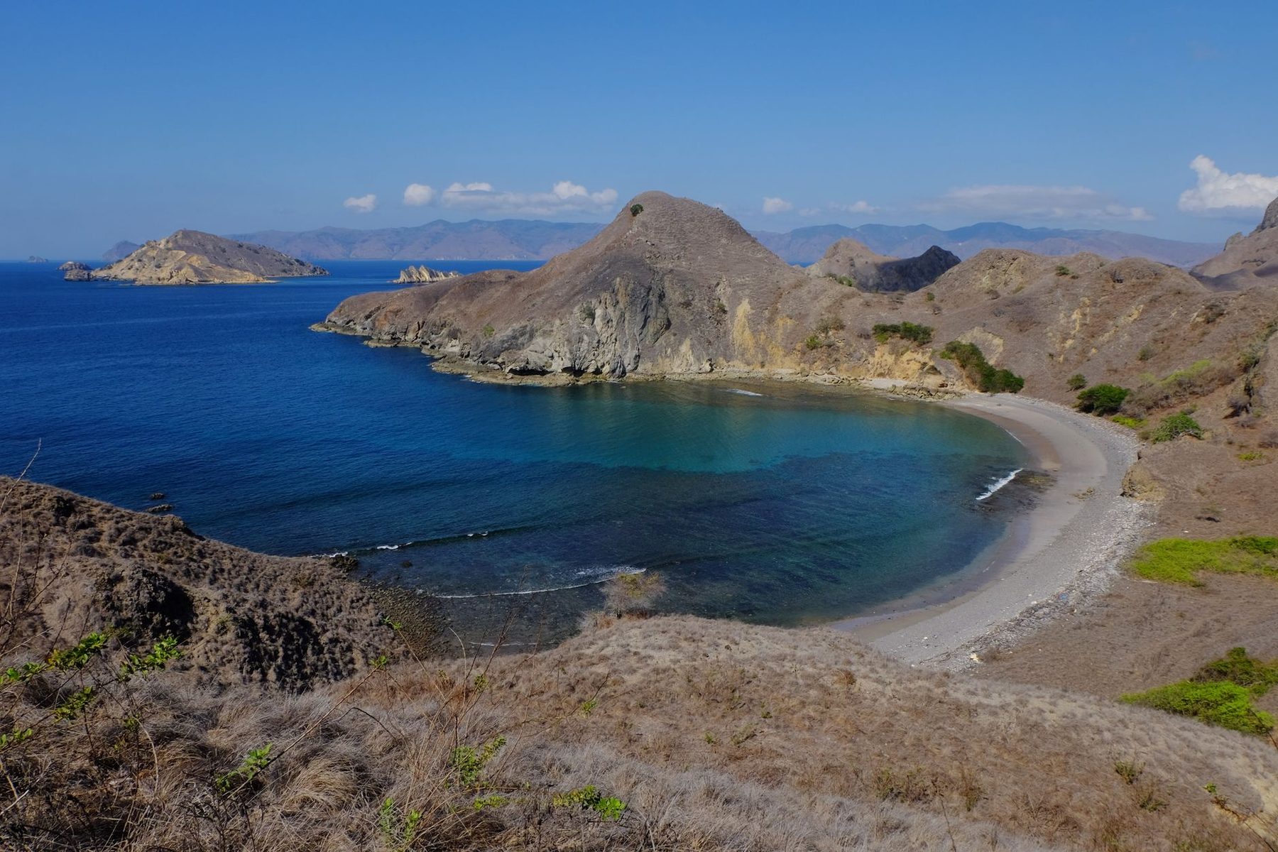Pemandangan pantai Pulau Padar dengan air jernih dan bukit berbatu di bawah langit cerah