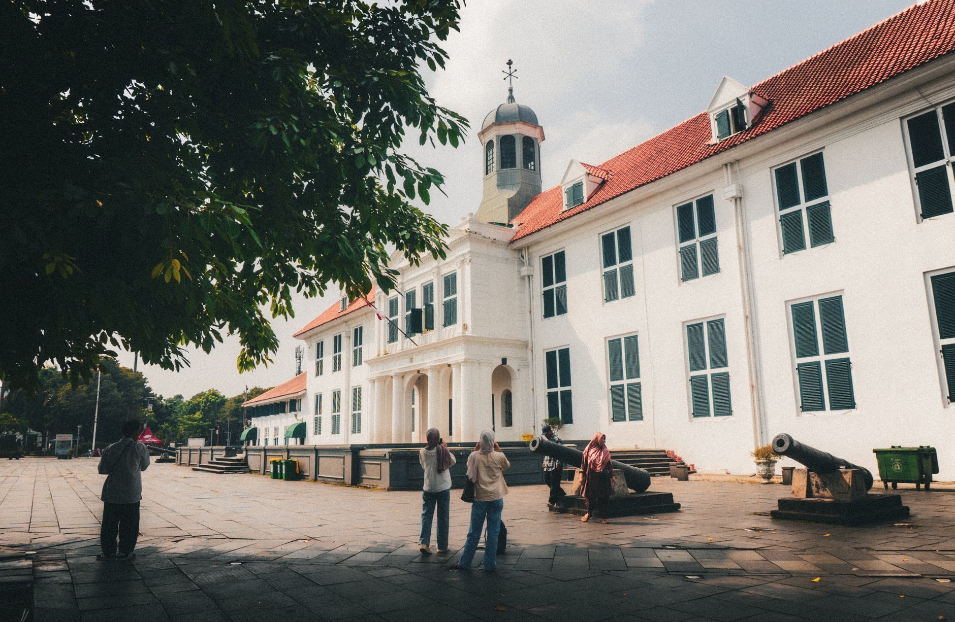 Bangunan bersejarah bergaya kolonial di Kota Tua Jakarta dengan pengunjung dan meriam di halaman depan